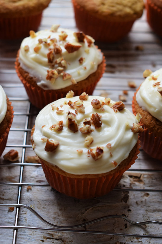 Pumpkin cupcakes with cream cheese frosting and pecans on a cooling rack