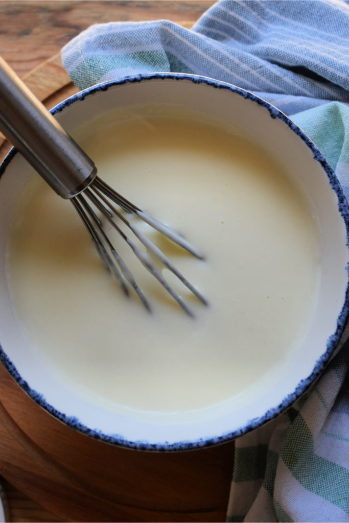 roux sauce in a bowl with a whisk and a striped tea towel