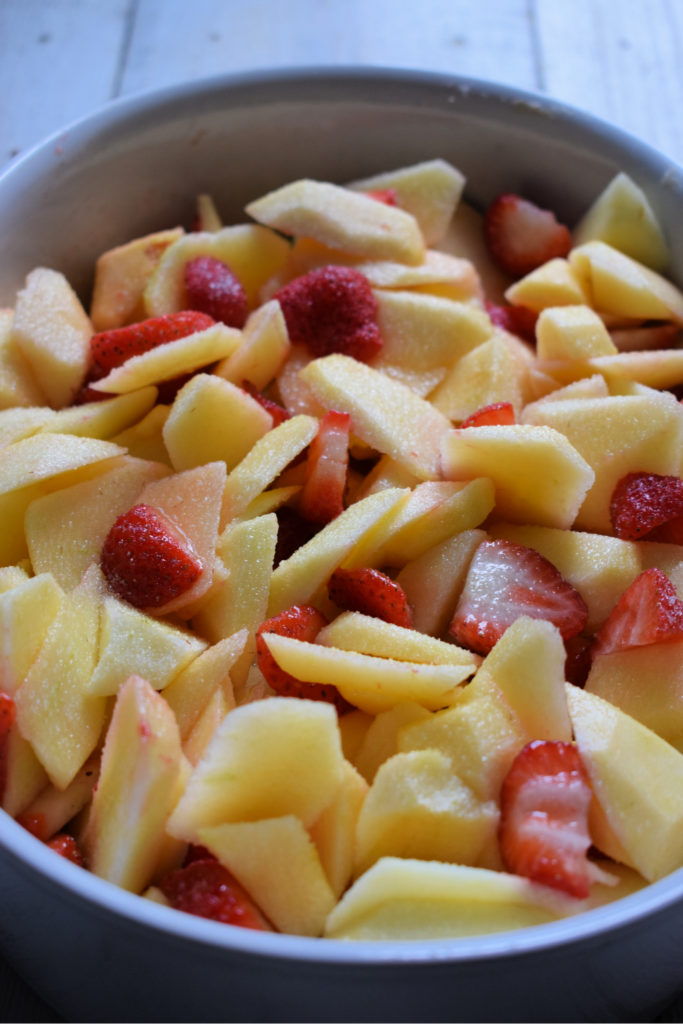 apples and strawberries cut up in a white baking dish