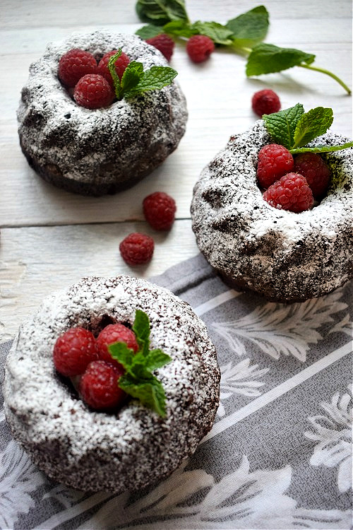 Mini Chocolate Bundt Cakes on a white table with raspberries