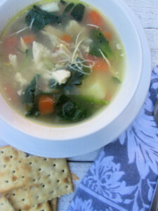 chicken and vegetable soup in a white bowl with crackers