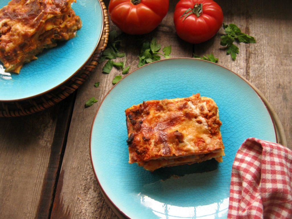 Clasic Lasagna on a wooden table with tomatoes.