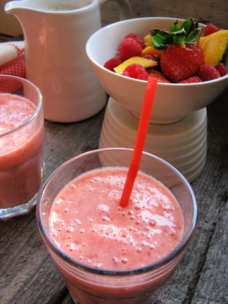 mango and berry smoothie in a glass with a straw