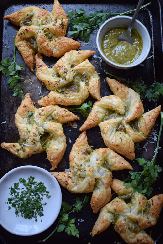 Pesto Puff Pastry Pinwheels on a baking tray with pesto and herbs