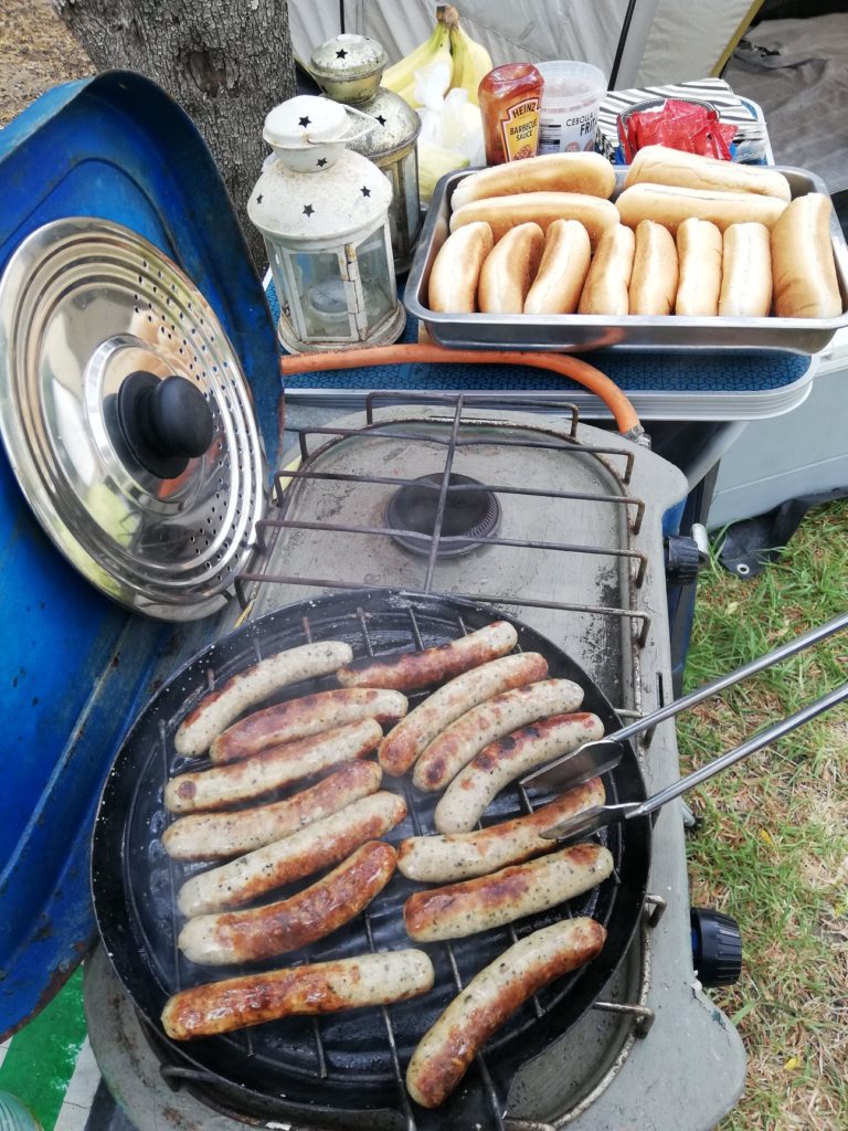 cooking sausages on a camp stove with hot dog buns