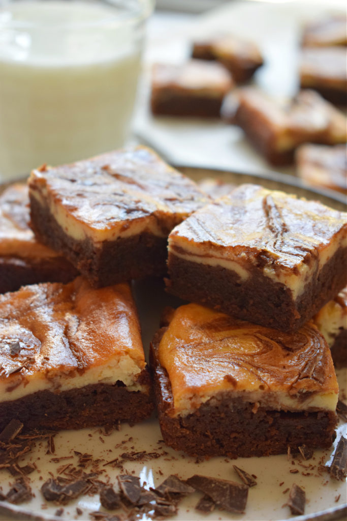 Cream Cheese Brownies stacked on a plate with a glass of milk in the background