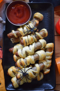 Halloween Mummy Sausage Rolls on a black plate