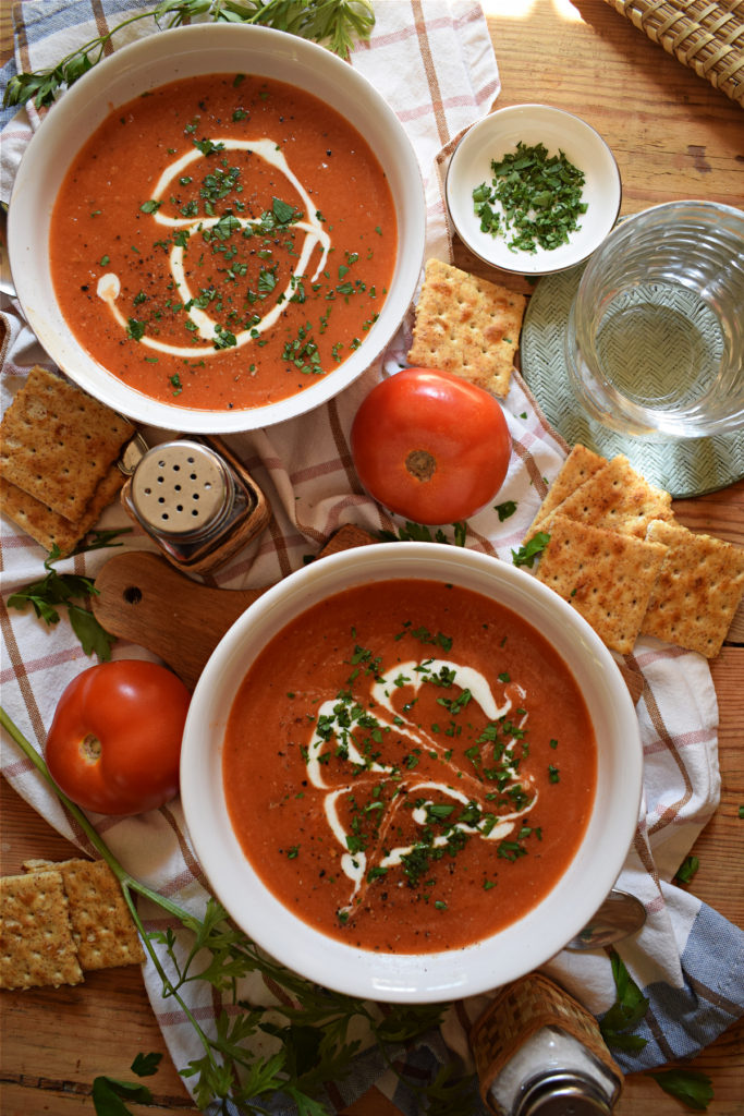 over head table setting view of the slow cooker tomato soup with fresh tomatoes and cream