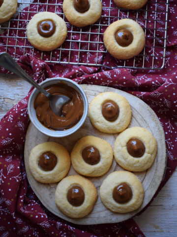 view of the dulce de leche thumbprint cookies on a wooden baord and baking rack