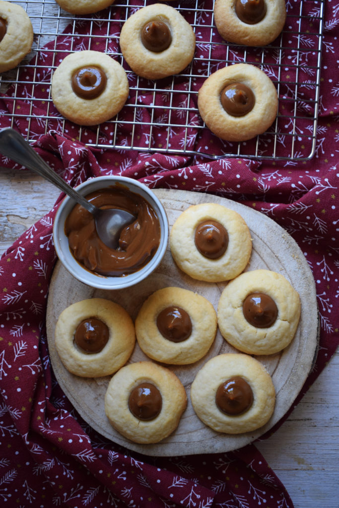 view of the dulce de leche thumbprint cookies on a wooden baord and baking rack