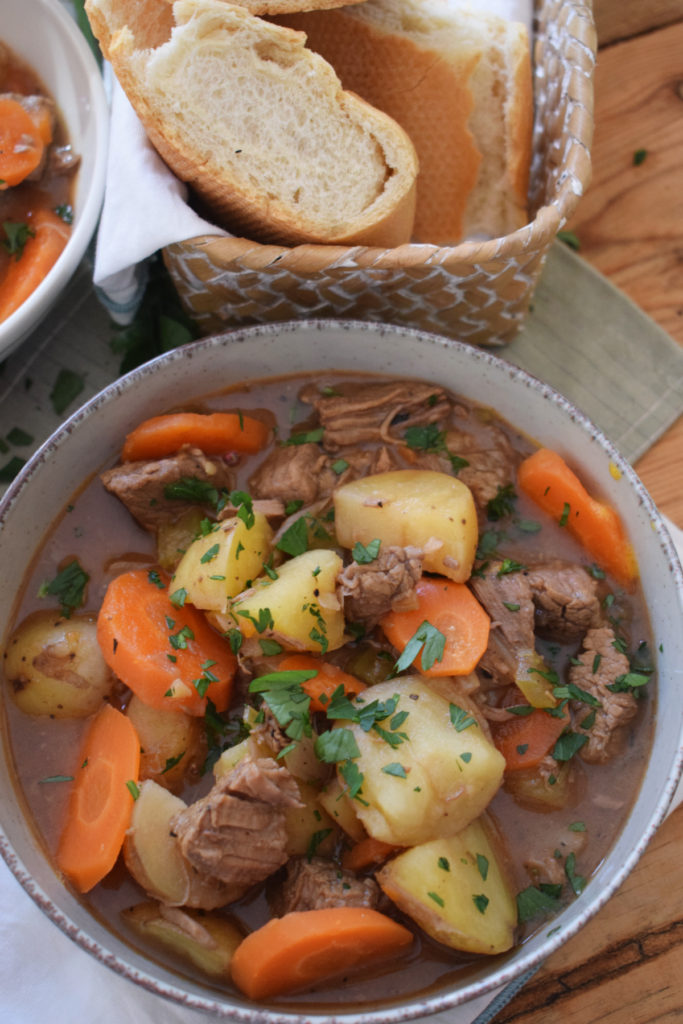 beef and vegetable stew in a bowl with bread on the side