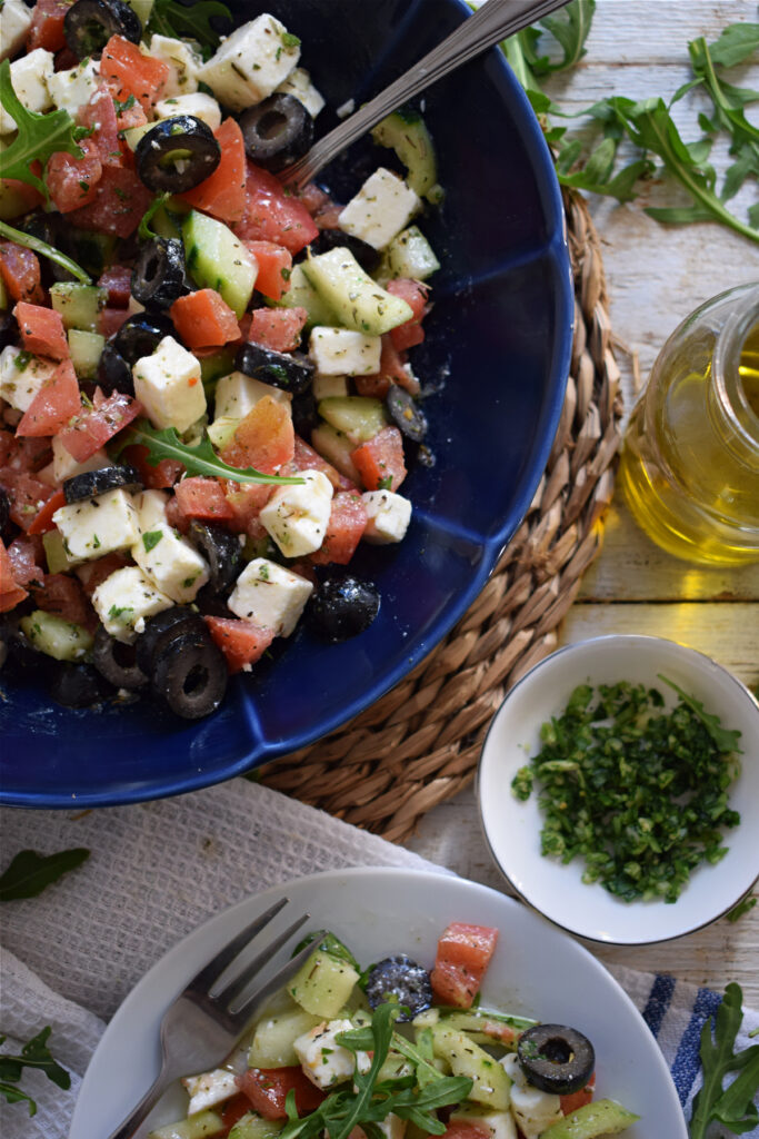 greek style  salad with marinaded feta in a blue bowl with dressing on the side