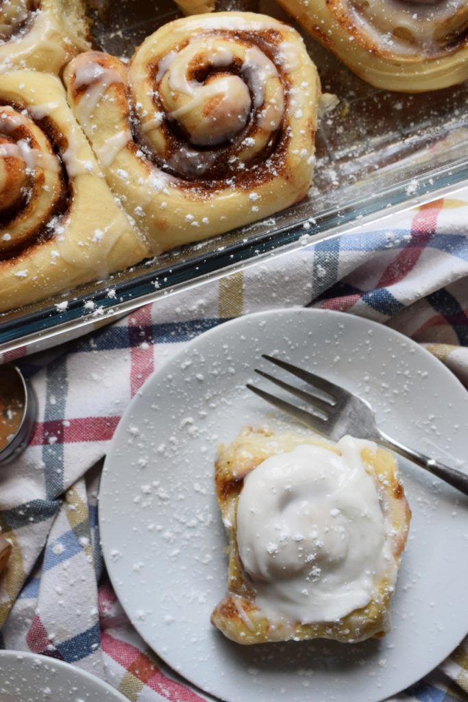 cinnamon roll on a plate with more cinnamon rolls in a baking tray