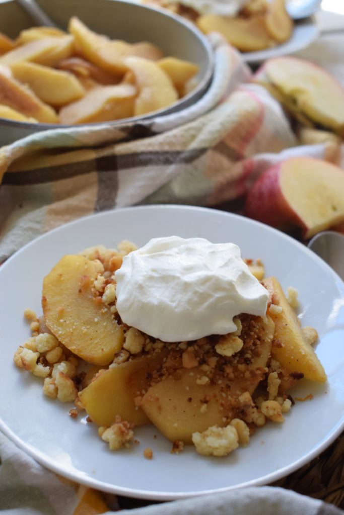 stove top apple crumble on a plate with whipped cream.