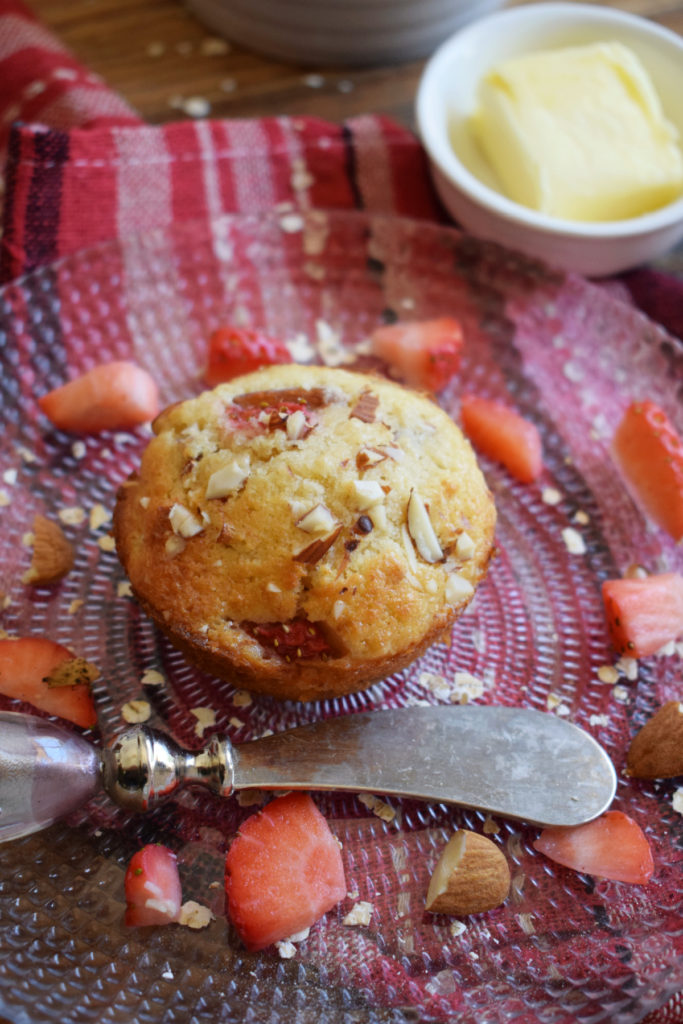 Strawberry muffin on a plate with fresh strawberries and butter.