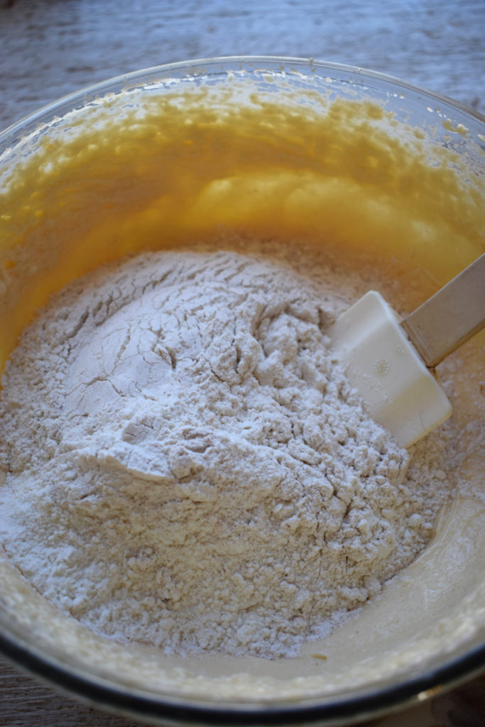 Flour being added to cake batter in a glass bowl.