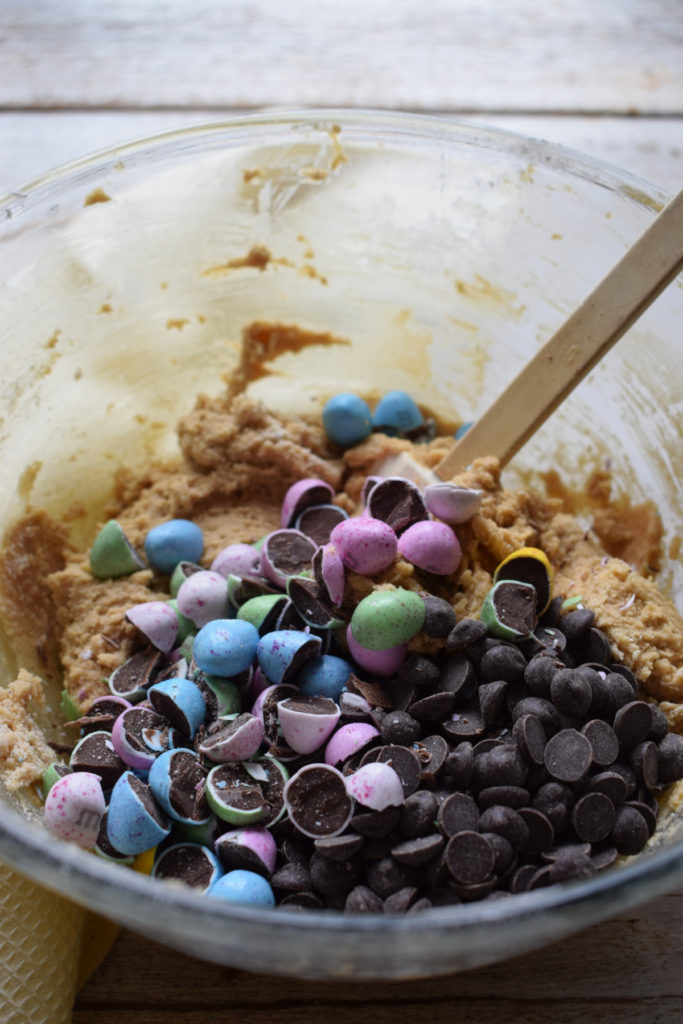 Adding chocolate chips and chopped mini eggs to cookie dough.