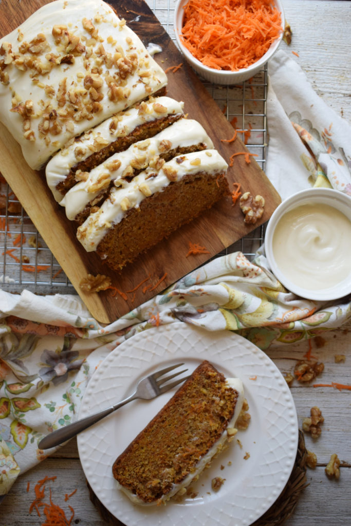 Carrot loaf cake on a wooden board with a slice on a plate and a floral napkin.