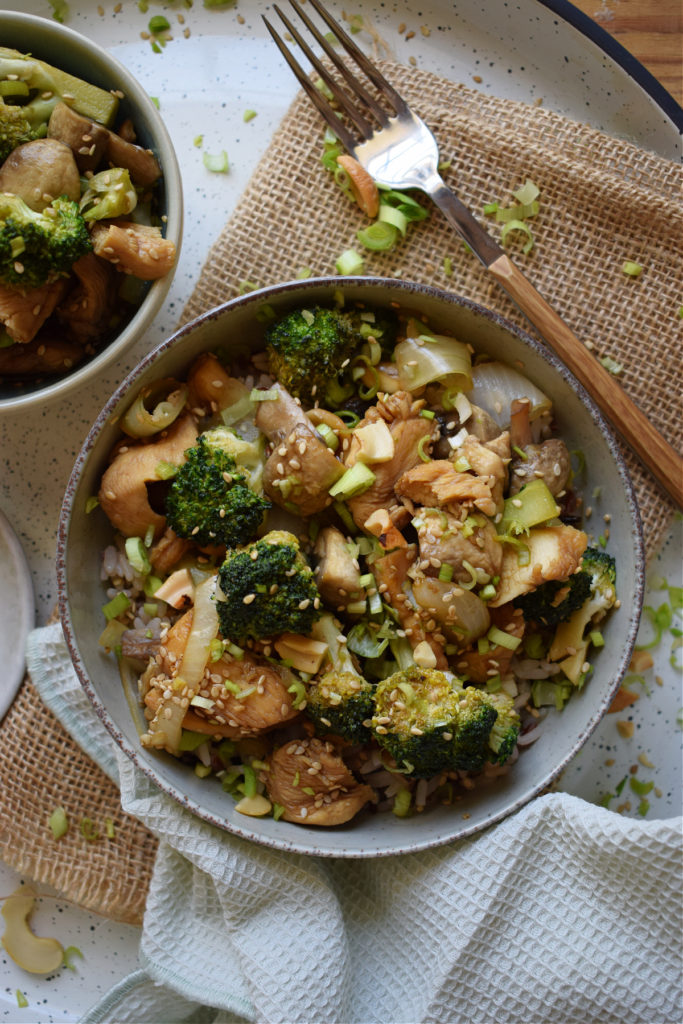 Chicken and broccoli stir fry in a bowl with a green napkin and fork.