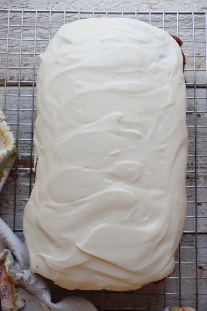 Cream cheese frosting on a carrot loaf cake on a cooling rack.