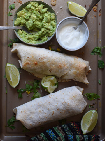 chicken and rice wraps on a baking sheet with sour cream and guacamole.