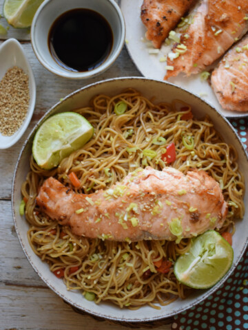 Salmon and noodles in a towl with teriyaki sauce on the side.