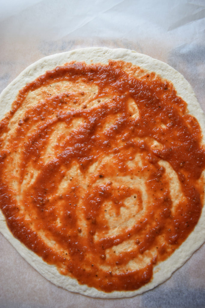 Adding pizza sauce to pizza dough.