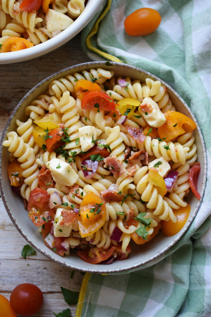 Bacon Tomato Pasta Salad in a bowl with a green and white tea towel.