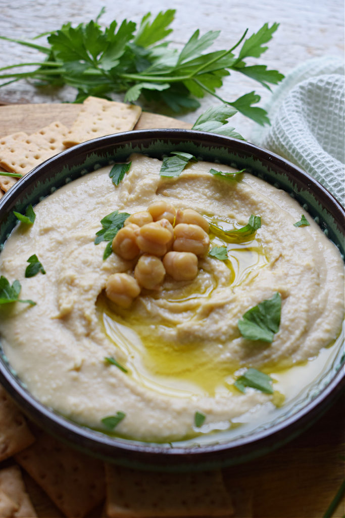 Hummus in a bowl with parsley garnish in the background.