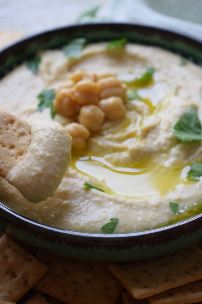 Hummus in a serving dish with chicpeas, olive oil and parsley on top.