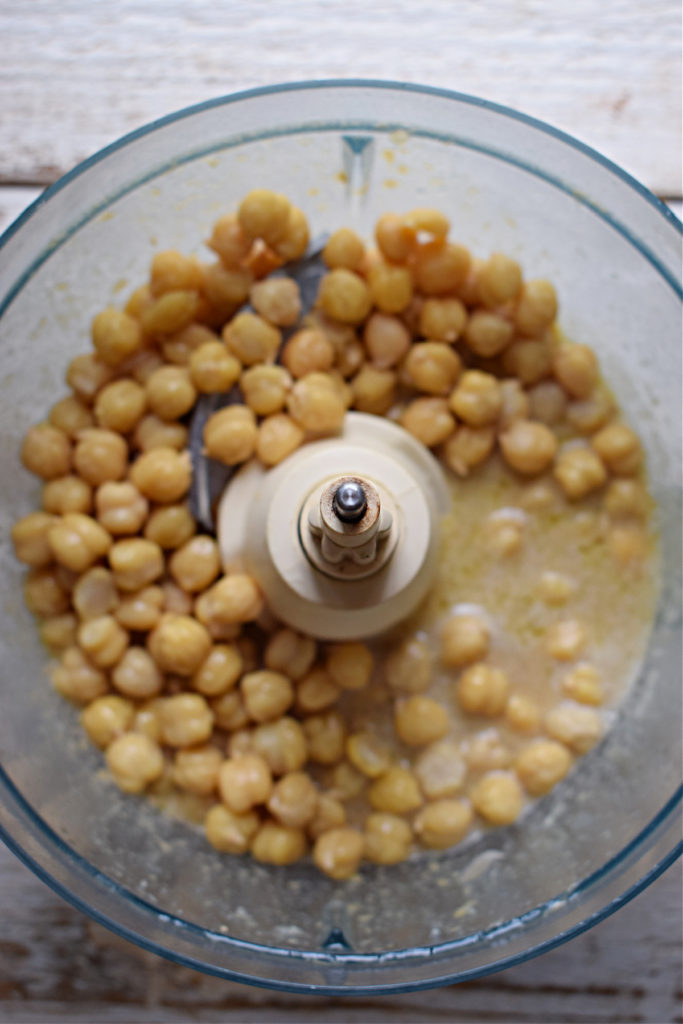 Adding chickpeas to a food processor to make hummus.