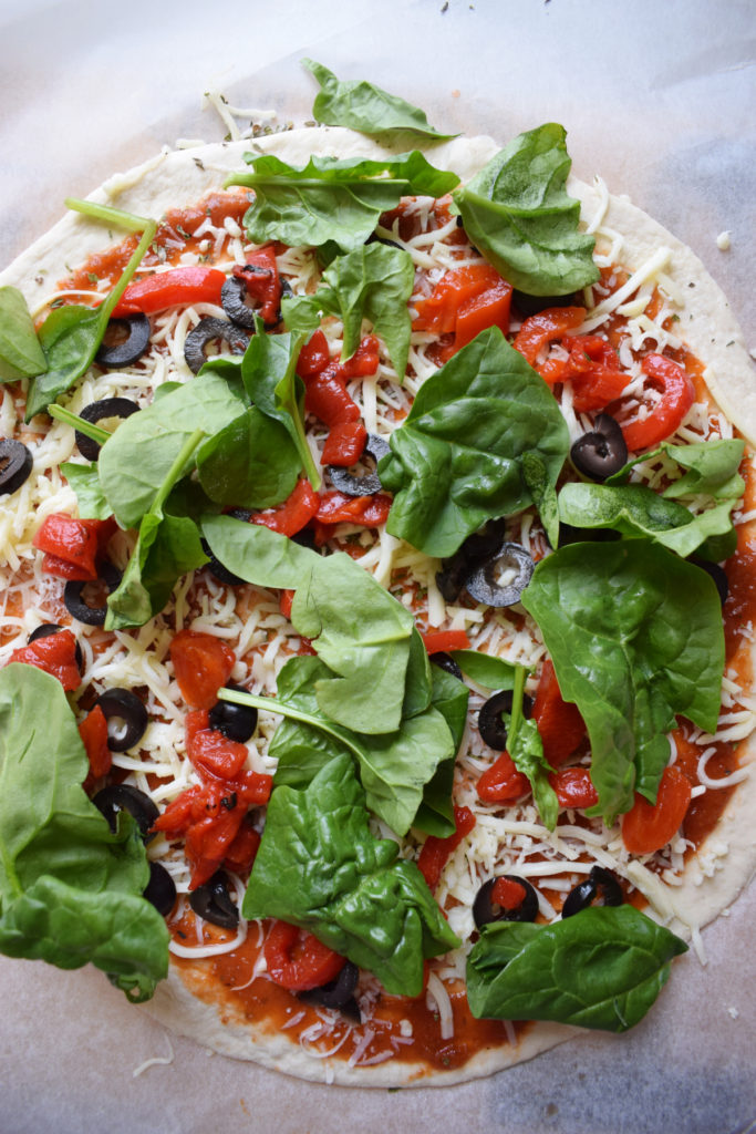 Top the pizza with roasted peppers, black olives and fresh spinach.