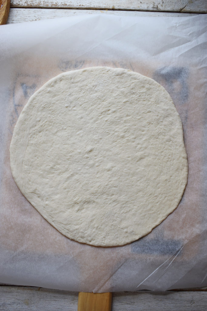 Pizza dough rolled out on a sheet of parchment paper.