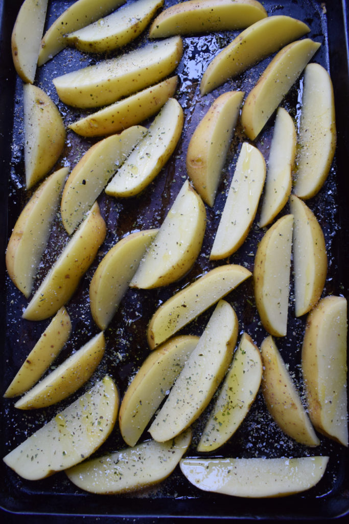 Potato wedges on a baking tray with seasonings.