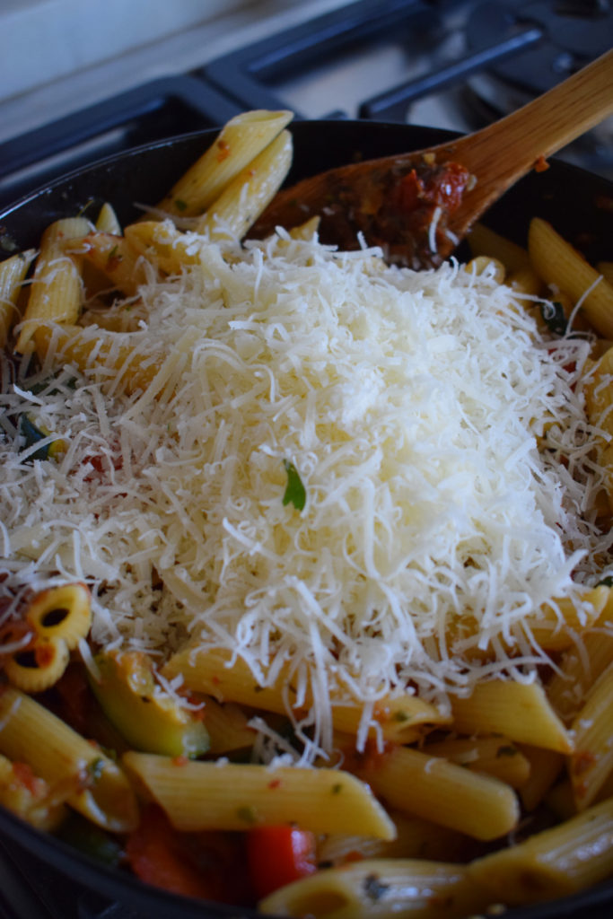 Adding parmesan cheese to a skillet with pasta.