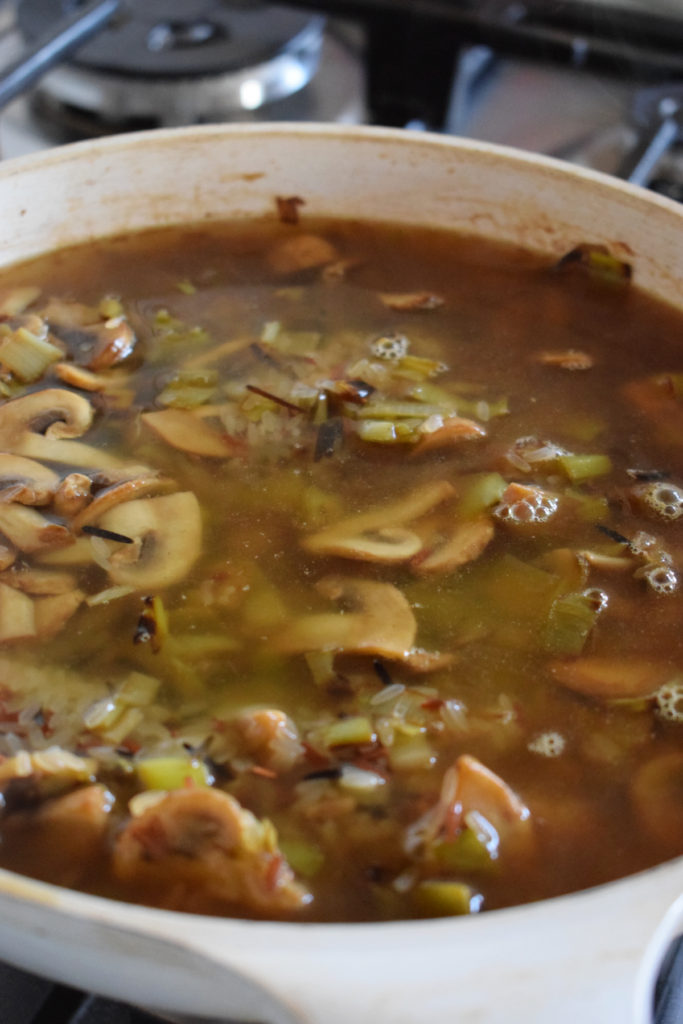 Adding vegetable broth to wild rice in a skillet.