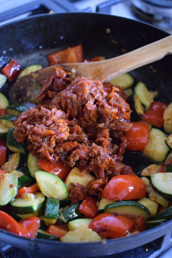 Cooked vegetables in a skillet with sun dried tomatoes.