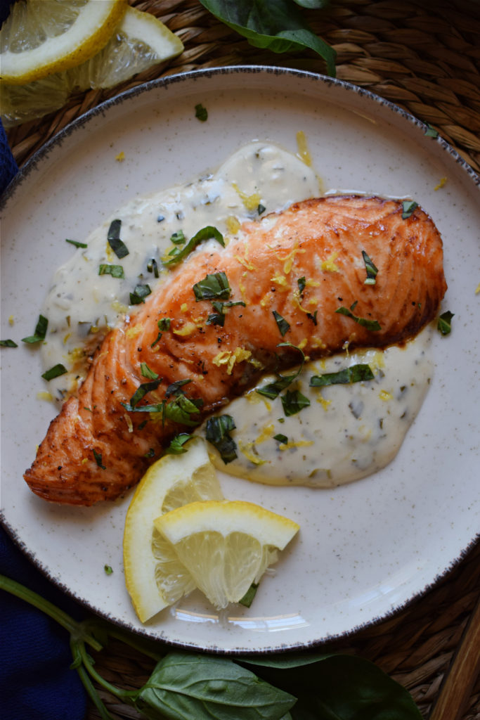 Baked salmon on a plate with sauce and lemon slices.
