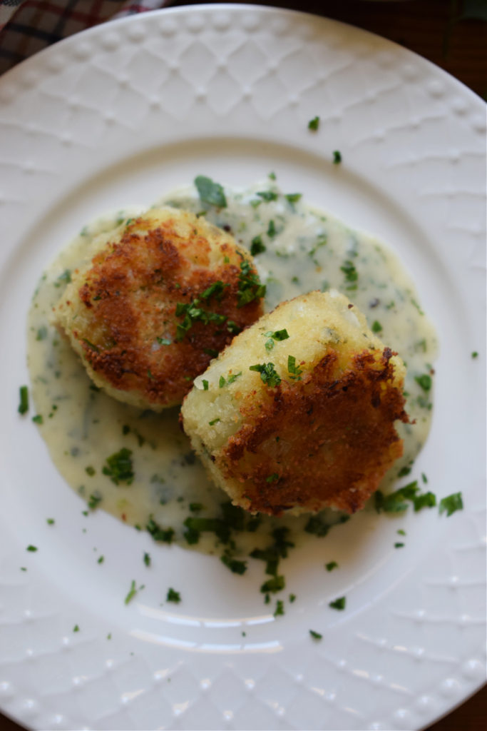 Cod cakes on a plate with parsley sauce.