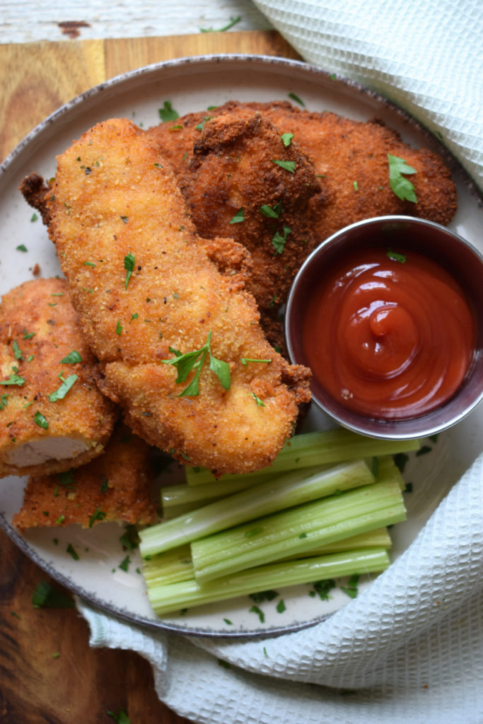 Chicken tenders on a plate with dipping sauce and celery.