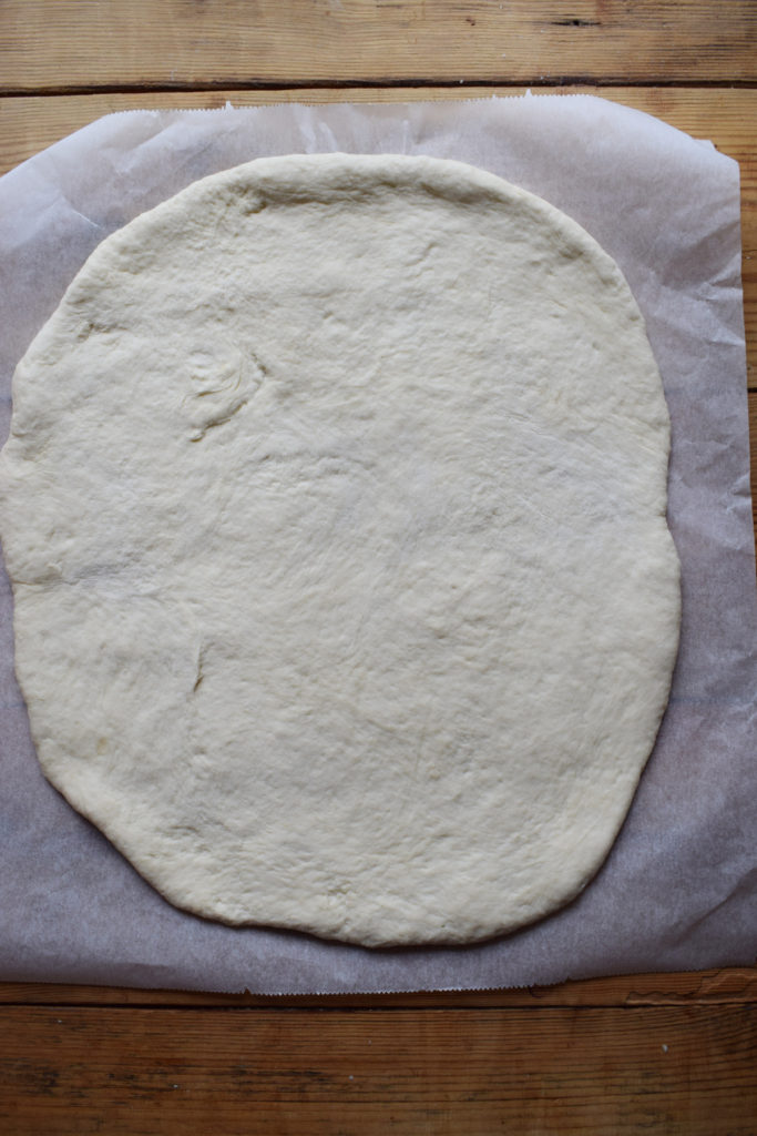 Pizza dough rolled out on parchment paper.