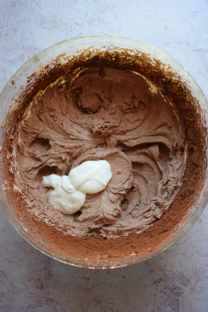Adding heavy cream to chocolate buttercream frosting.