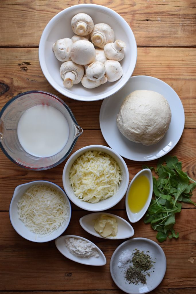 Ingredients on a wooden table to make an alfredo pizza.
