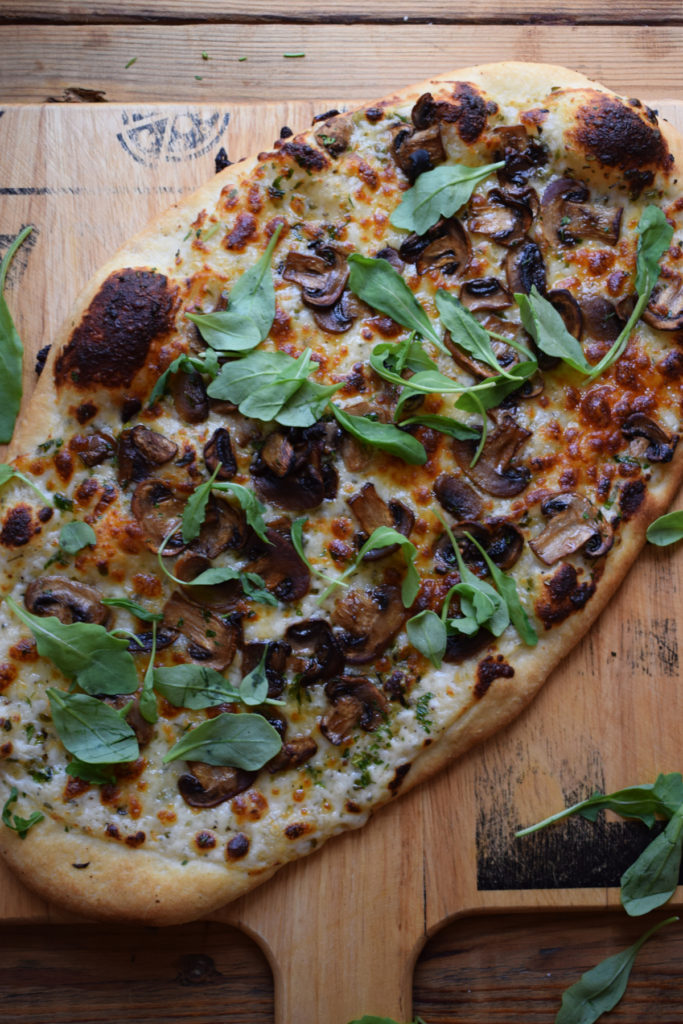Cooked Alfredo mushroom pizza on a pizza board.
