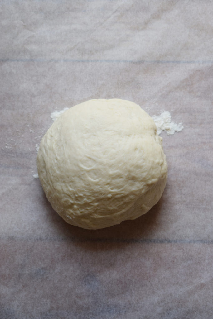 A pizza dough ball on a sheet of parchment paper.