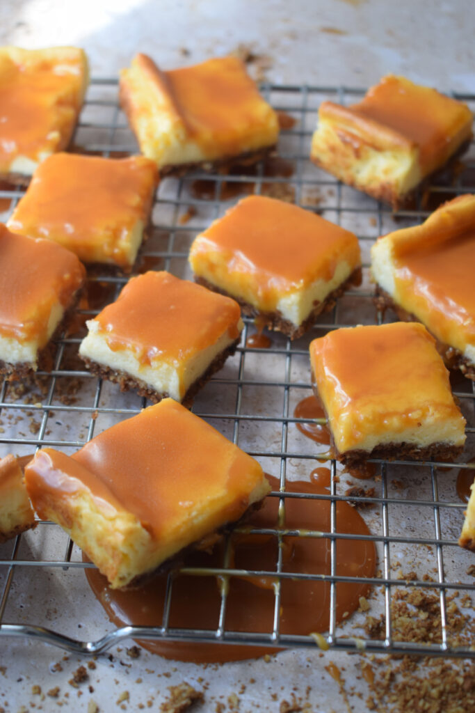 Caramel topped cheesecake squares on a rack.