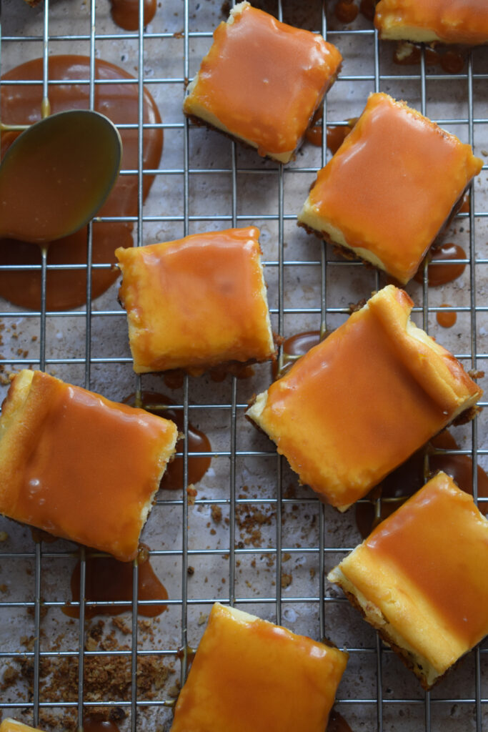 Caramel topped cheeseckae squares on a rack.