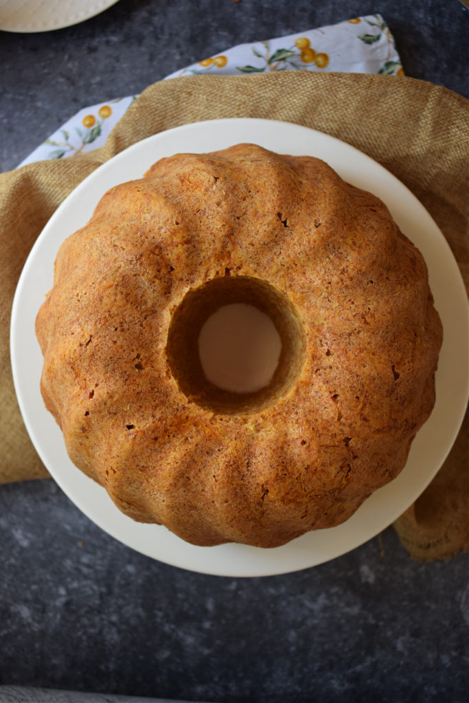 Over head view of a plain carrot bundt cake on a white plate with a dark background.