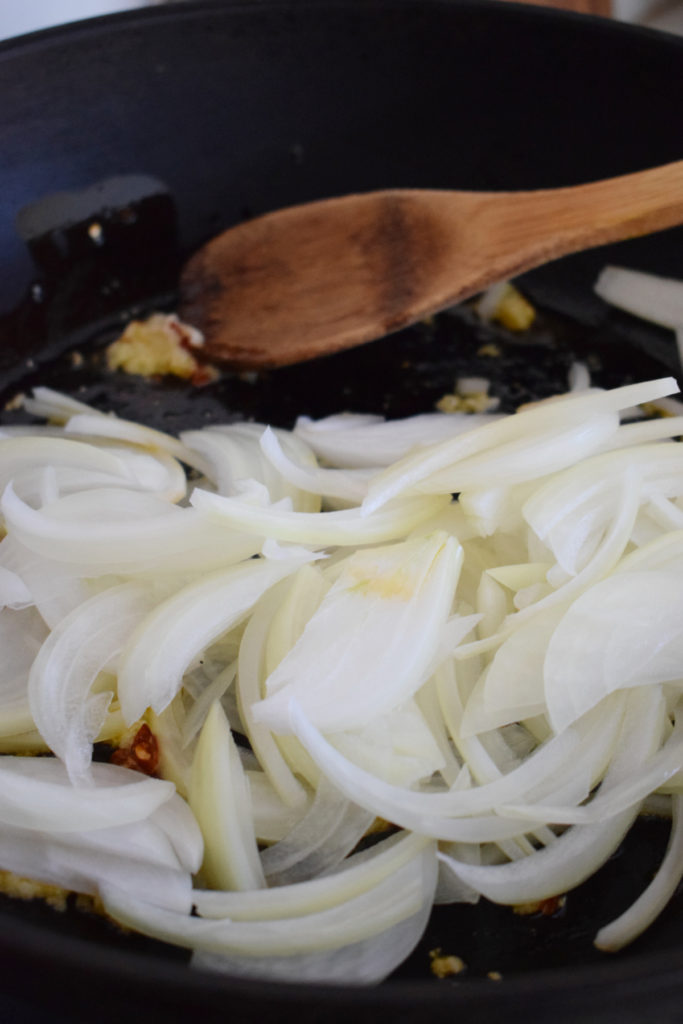 Adding onions to a skillet.