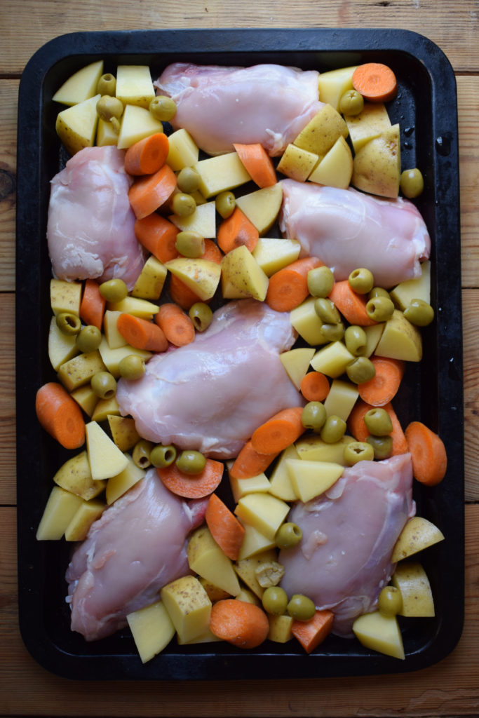Chicken, vegetables and olives on a baking tray.